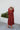 Full body back view of model wearing the Seasons Change Maxi Dress, which has a rust colored fabric, a V neckline, long sleeves, a button-up front, a babydoll design, a midi length, and a flowy fit.