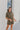 Frontal view of the The Lady May Romper that features an olive green fabric, a collar neckline, a short cuffed sleeve, a button-up front, two front pockets at the chest, a cuffed bottom hem, and two back pockets.