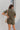 Back view of the The Lady May Romper that features an olive green fabric, a collar neckline, a short cuffed sleeve, a button-up front, two front pockets at the chest, a cuffed bottom hem, and two back pockets.