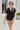 Frontal view of the Irreplaceable Top that features a black colored material, a round neckline with a ruffle detail, a tie detail with a cut-out at the chest, a short sleeve, and a fowy fit