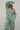 Front view of model wearing the Having A Good Day Pants that have turquoise plisse fabric with a multicolor floral pattern, a ruffled hem, a cropped waist, a button-up front, a collar, and long sleeves.