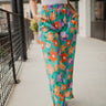 Front view of model wearing the Having A Good Day Pants that have turquoise plisse fabric with a multicolor floral pattern, a ruffled hem, a cropped waist, a button-up front, a collar, and long sleeves.