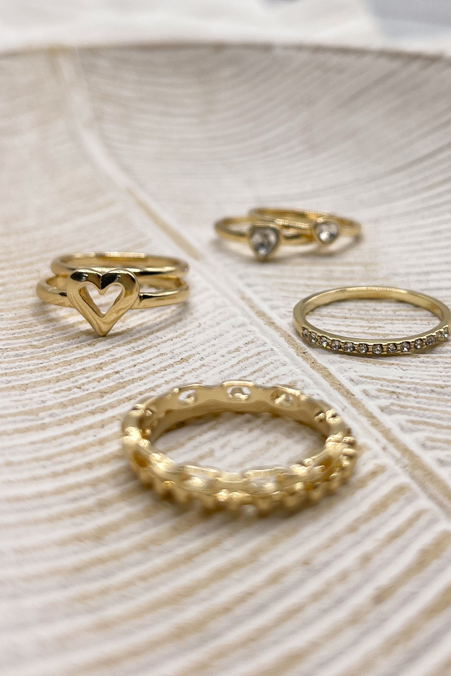 Image shows rings in the Veronica Heart Ring Set in Gold. Rings are in 4 stacks against a beige backdrop.