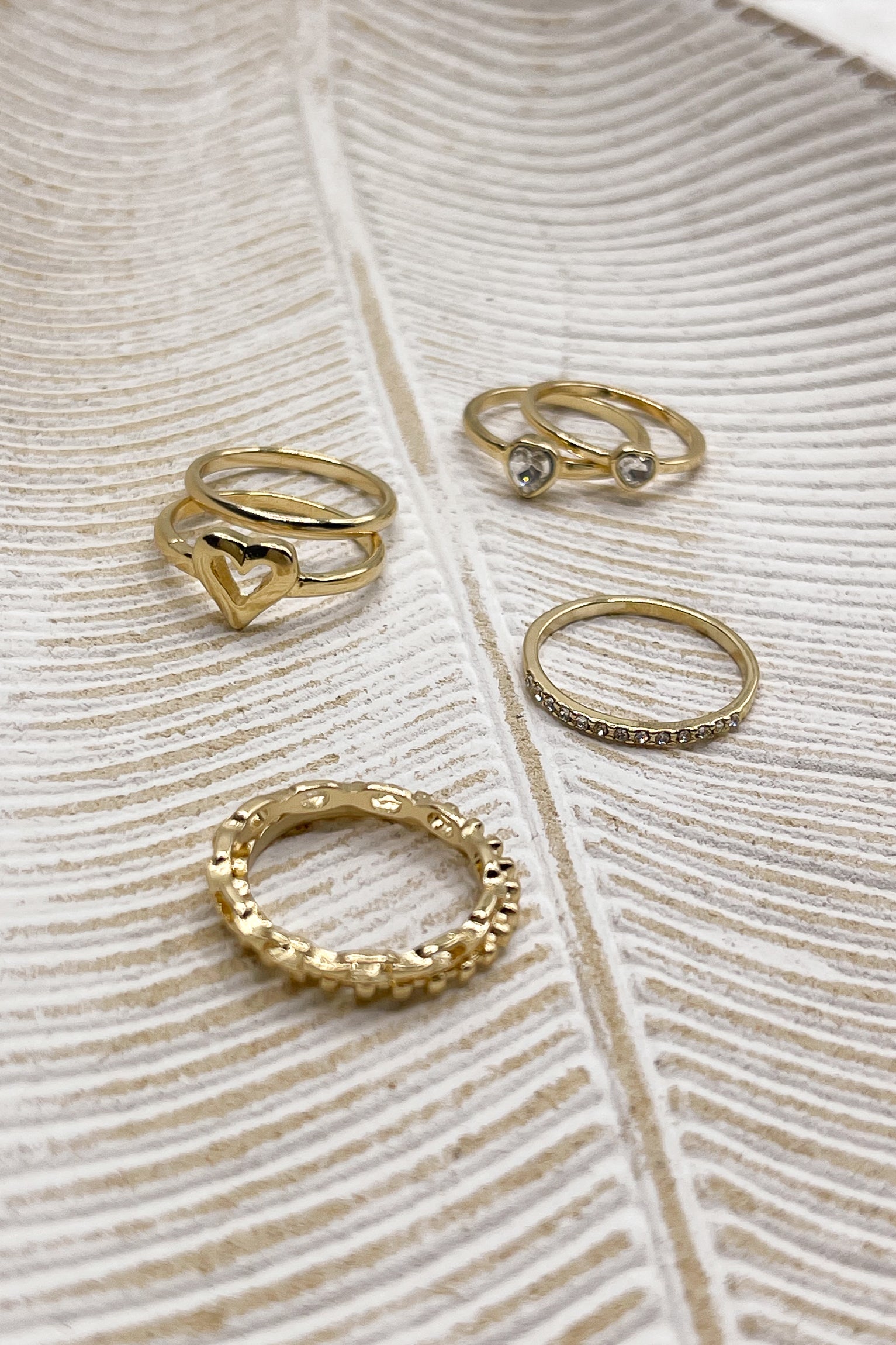 Image shows rings in the Veronica Heart Ring Set in Gold. Rings are in 4 stacks against a beige backdrop.