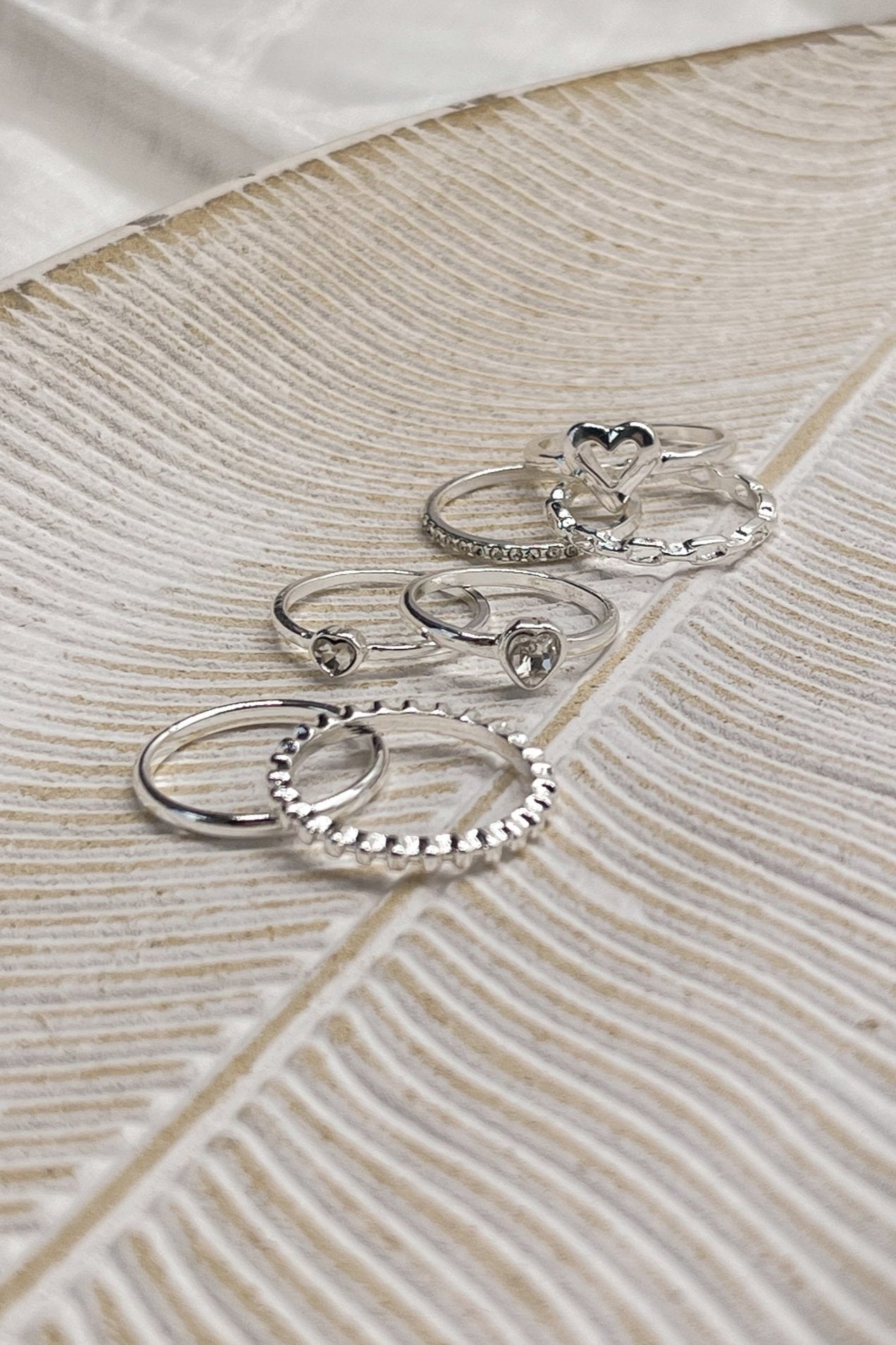 Image shows rings in the Veronica Heart Ring Set in Silver. Rings are in 3 stacks against a beige backdrop.