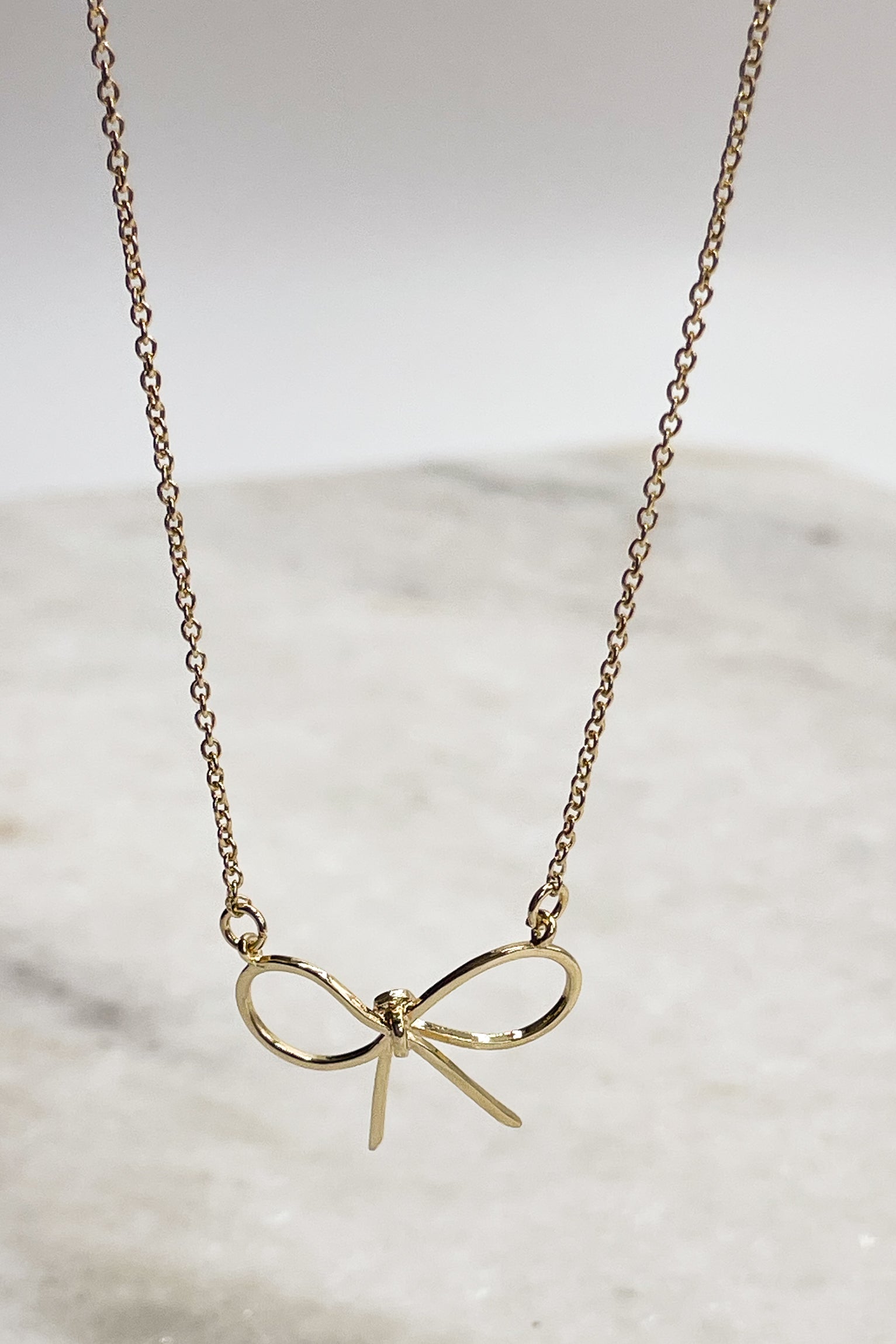 Close up of bow on Gabriella Gold Bow Necklace, adjustable gold chain link with a gold wire bow attachment.