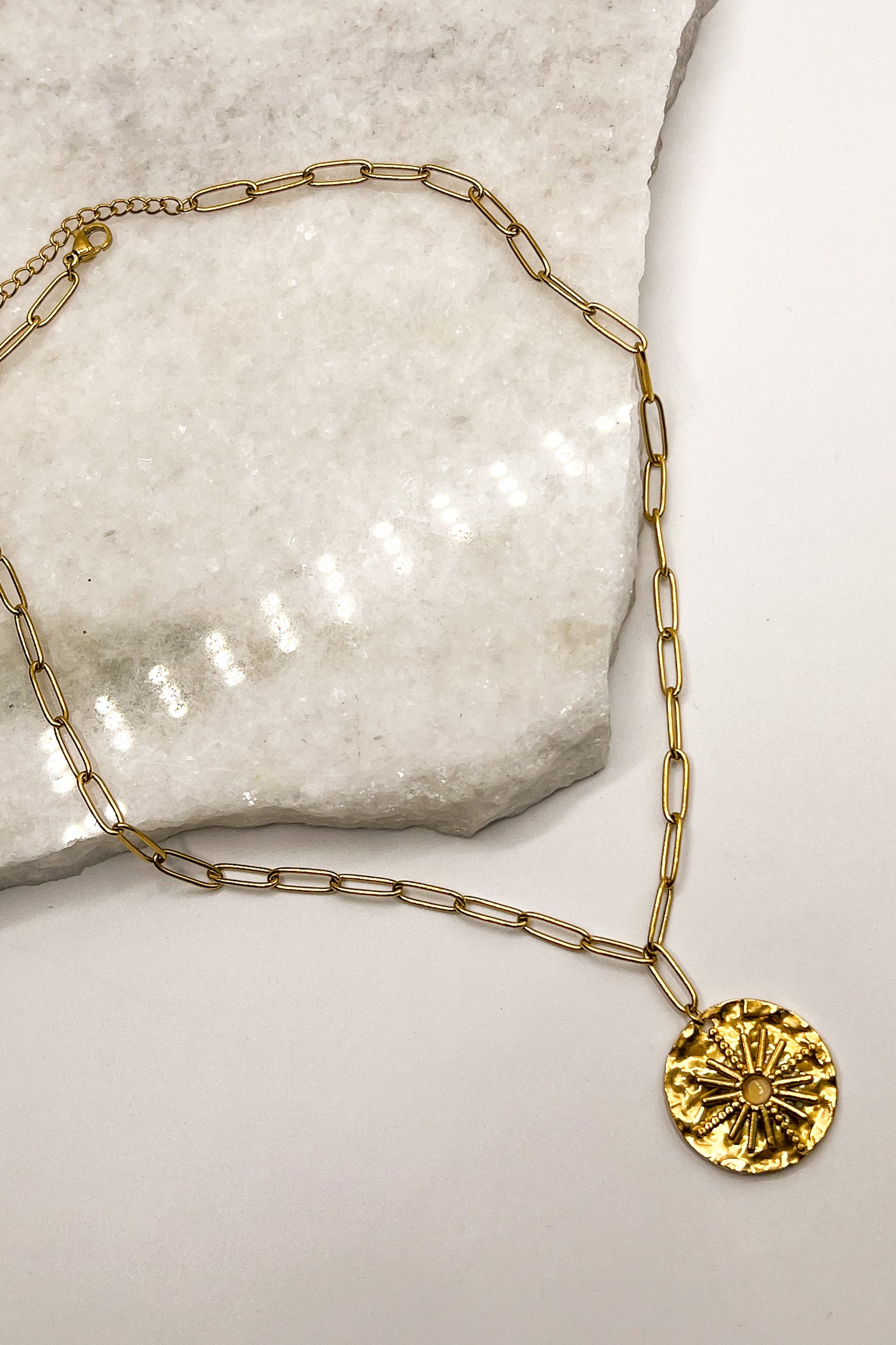 flat lay view of the Starburst Gold Chain Link Necklace which features adjustable gold chain link with a hammered medllaion and starburst detail