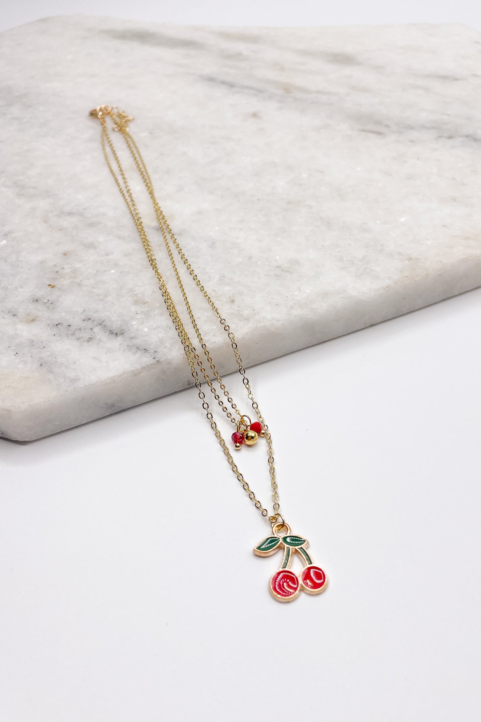 Close up of Aria Cherry Gold Necklace. This is a layered gold necklace with cherries and red beads.