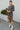 Full body front view of model wearing the Keep Your Cool Dress , which has a grey ribbed material, a round neck, long sleeves, a front knot detail, a front slit, and a high-low silhouette.