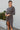 Full body front view of model wearing the Keep Your Cool Dress , which has a grey ribbed material, a round neck, long sleeves, a front knot detail, a front slit, and a high-low silhouette.