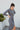 Side view of model wearing the Keep Your Cool Dress, which has a grey ribbed material, a round neck, long sleeves, a front knot detail, a front slit, and a high-low silhouette.