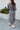 Back view of model wearing the Keep Your Cool Dress, which has a grey ribbed material, a round neck, long sleeves, a front knot detail, a front slit, and a high-low silhouette.