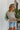 Side view of model wearing the Hamptons Striped Sweatshirt, which features a cream colored material, a black stripe pattern, a rounded green ribbed neckline, and long sleeves with green ribbed cuffs.