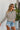 Front view of model wearing the Hamptons Striped Sweatshirt, which features a cream colored material, a black stripe pattern, a rounded green ribbed neckline, and long sleeves with green ribbed cuffs.