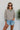 Front view of model wearing the Hamptons Striped Sweatshirt, which features a cream colored material, a black stripe pattern, a rounded green ribbed neckline, and long sleeves with green ribbed cuffs.