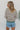 Back view of model wearing the Hamptons Striped Sweatshirt, which features a cream colored material, a black stripe pattern, a rounded green ribbed neckline, and long sleeves with green ribbed cuffs.