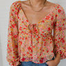 Close-up front view of model wearing the Take Me Back Floral Top, which features a chiffon material, a multi-colored floral print, a V neckline with a tie detail, a front cut-out, long sleeves, and a smocked back