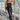 Front view of model wearing The Hailey Jumpsuit features black faux-leather, a sleeveless design, a straight neckline, a tie belt at the waist, a back zipper closure, and a straight leg fit.
