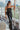 Front view of model wearing The Hailey Jumpsuit features black faux-leather, a sleeveless design, a straight neckline, a tie belt at the waist, a back zipper closure, and a straight leg fit.