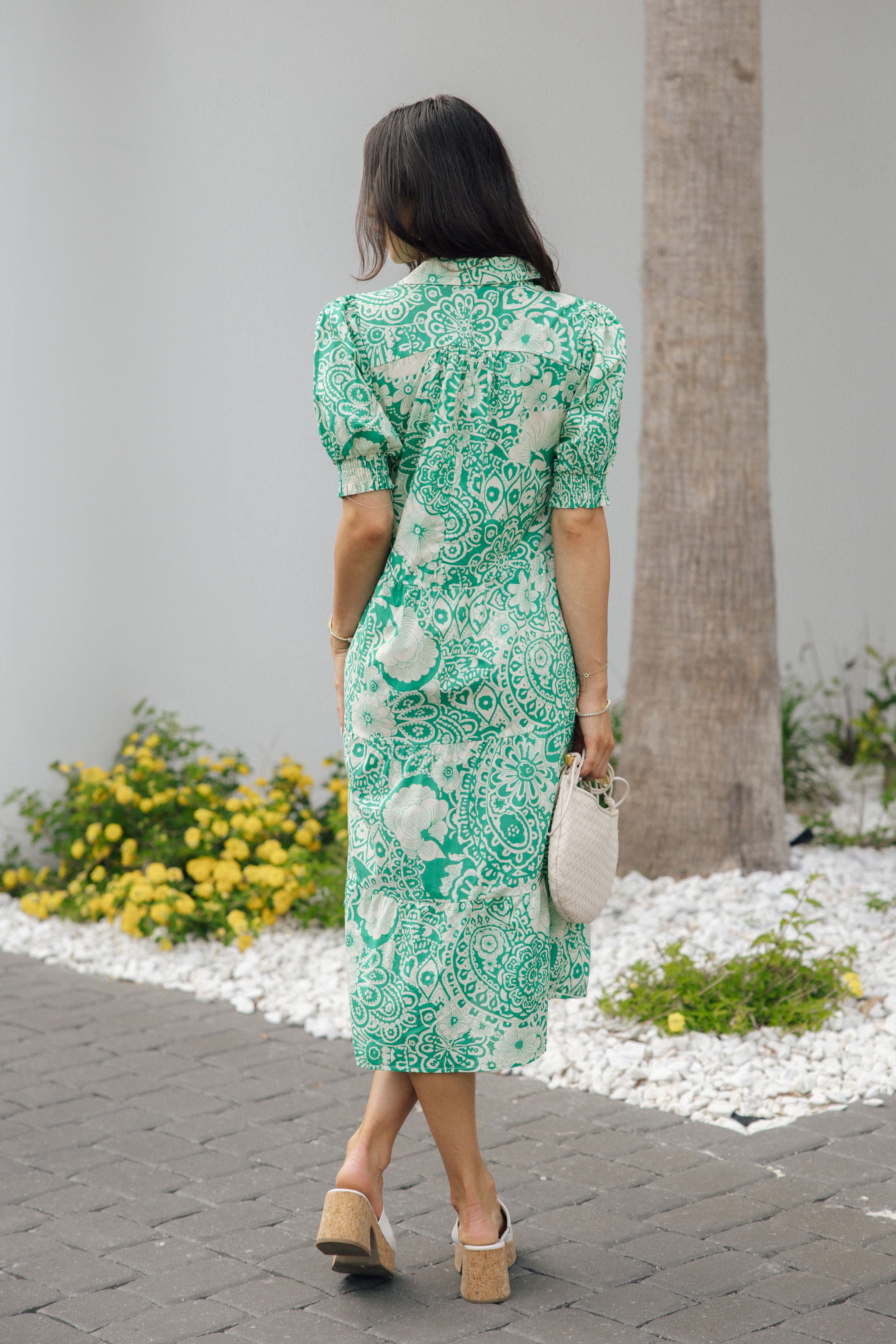 Full body back view of female model wearing the Celeste Green & Cream Floral Paisley Midi Dress which features Green and Cream Floral Paisley Pattern, Midi Length, Tiered Body, V-Neckline with Collar and Short Puff Sleeves