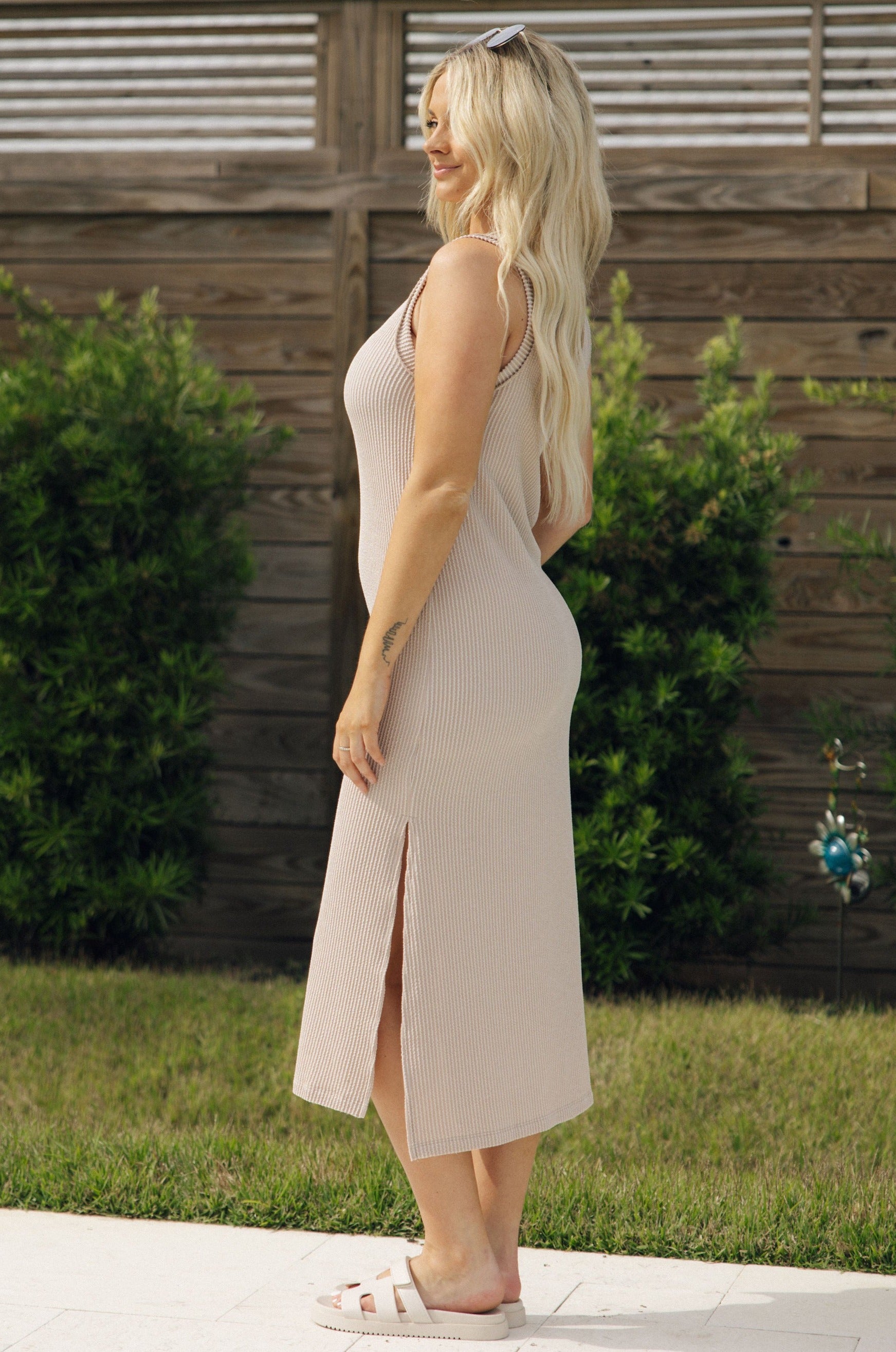 Full body side view of female model wearing the Everly Light Taupe Ribbed Sleeveless Midi Dress which features Light Taupe Ribbed Fabric, Midi Length, Slit On The Side, Round Neckline and Sleeveless