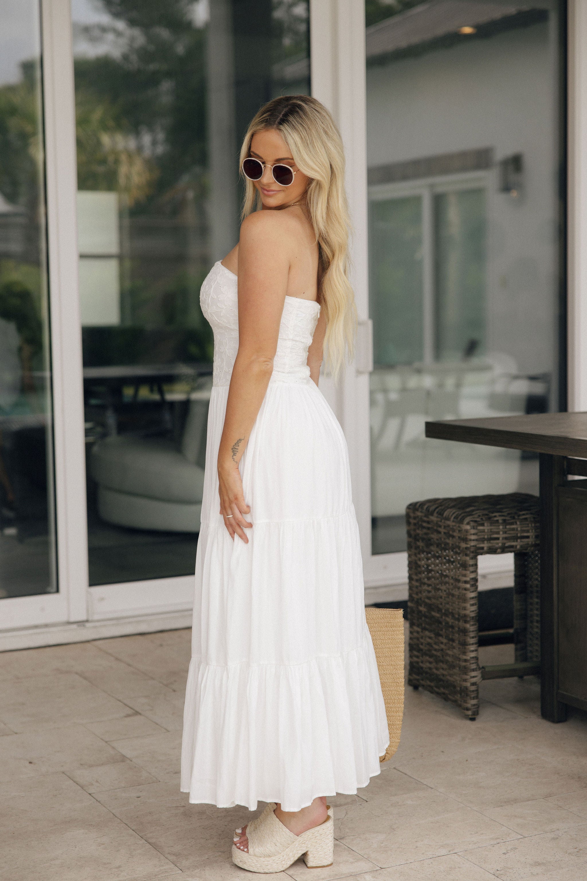 Full body side view of model wearing the Paloma White Eyelet Strapless Maxi Dress that has a strapless upper with eyelet and floral details and a tiered maxi skirt.