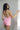 Back view of female model wearing the Palmer Pink Ruffle Halter Sleeveless Romper which features Pink Lightweight Fabric, Pink Shorts Lining, Surplice Neckline with Halter Neck Ties, Ruffle Hem Details, Open Back and Back Zipper with Hook Closure