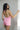 Back view of female model wearing the Palmer Pink Ruffle Halter Sleeveless Romper which features Pink Lightweight Fabric, Pink Shorts Lining, Surplice Neckline with Halter Neck Ties, Ruffle Hem Details, Open Back and Back Zipper with Hook Closure