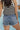 Back view of female model wearing the Rowyn Washed Denim Buttoned Pockets Shorts which features Medium Wash Denim Fabric, Folded Hem, Two Buttoned Front Pockets, Two Back Pockets, Front Zipper with Button Closure and Belt Loops