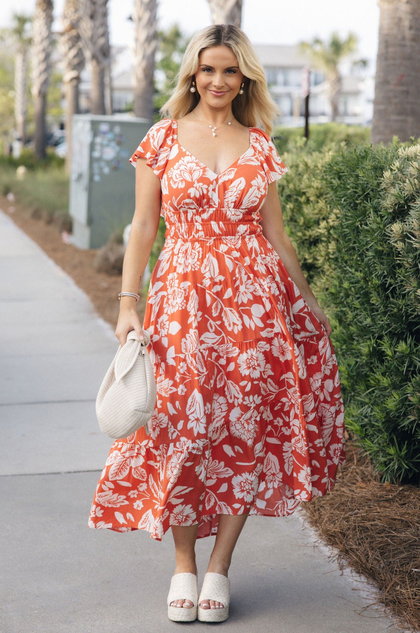 Full body view of female model wearing the Elena Orange & Cream Floral Midi Dress which features Orange and White Floral Design, Midi Length, Orange Thigh Length Lining, Tiered Body, Smocked Waistband, Sweetheart Neckline, Ruffle Straps and Open Back