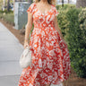 Full body view of female model wearing the Elena Orange & Cream Floral Midi Dress which features Orange and White Floral Design, Midi Length, Orange Thigh Length Lining, Tiered Body, Smocked Waistband, Sweetheart Neckline, Ruffle Straps and Open Back