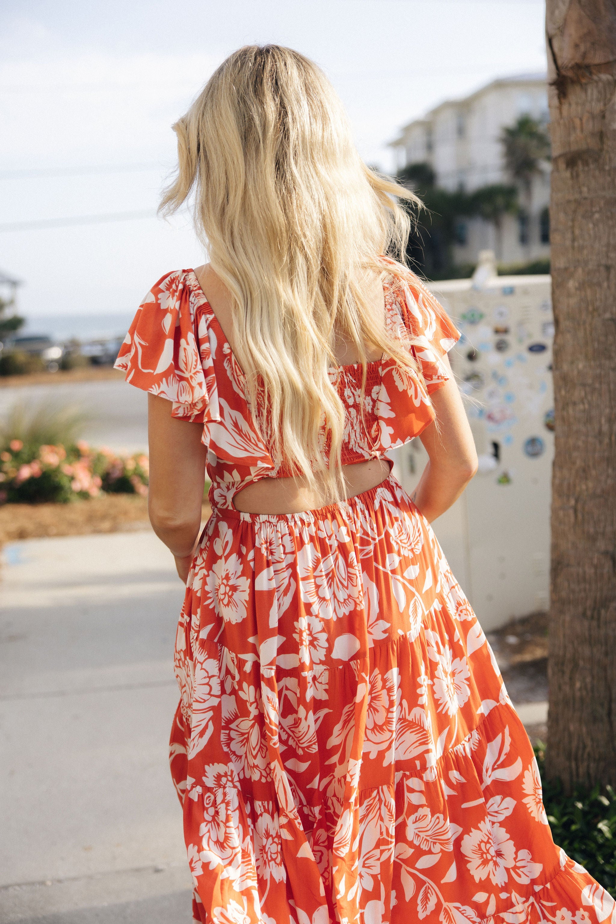 Back view of female model wearing the Elena Orange & Cream Floral Midi Dress which features Orange and White Floral Design, Midi Length, Orange Thigh Length Lining, Tiered Body, Smocked Waistband, Sweetheart Neckline, Ruffle Straps and Open Back