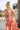 Back view of female model wearing the Elena Orange & Cream Floral Midi Dress which features Orange and White Floral Design, Midi Length, Orange Thigh Length Lining, Tiered Body, Smocked Waistband, Sweetheart Neckline, Ruffle Straps and Open Back