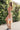 Full body side view of female model wearing the Lorelei Lavender & Orange Midi Dress that has a geometric lavender and orange print, midi length asymmetric hem, and thin straps,