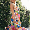 Full body side view of female model wearing the Avianna Orange Floral Maxi Dress that has orange, pink, green, and blue large florals, thin straps, ruffled hem, and ruched bust. Model is twirling in picture.
