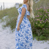 Full body side view of female model wearing the Camila White & Blue Floral Ruffle Maxi Dress which features Blue and White Floral Print, Maxi Skirt, Slit Detail, White Lining, Smocked Upper and Ruffle Straps