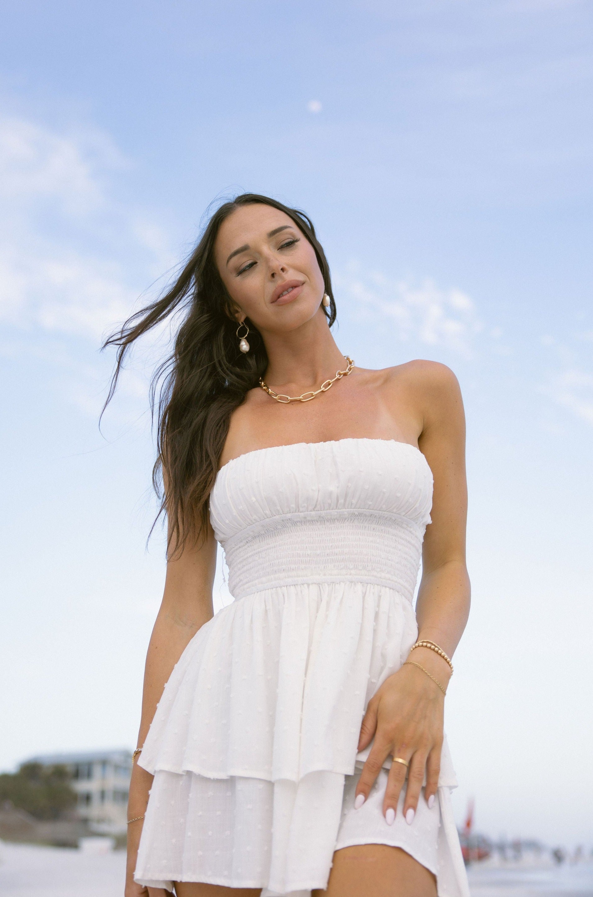 Upper body front view of female model wearing the Jemma White Swiss Dot Romper that has white swiss dot fabric, a strapless neck, and tiered shorts.