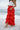 Lower body side view of female model wearing the Katrina Tiered Ruffle Maxi Skirt in Red that has tiered red fabric and an elastic waist. Worn with white top tucked in.
