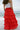 Lower body back view of female model wearing the Katrina Tiered Ruffle Maxi Skirt in Red that has tiered red fabric and an elastic waist. Worn with white top tucked in.