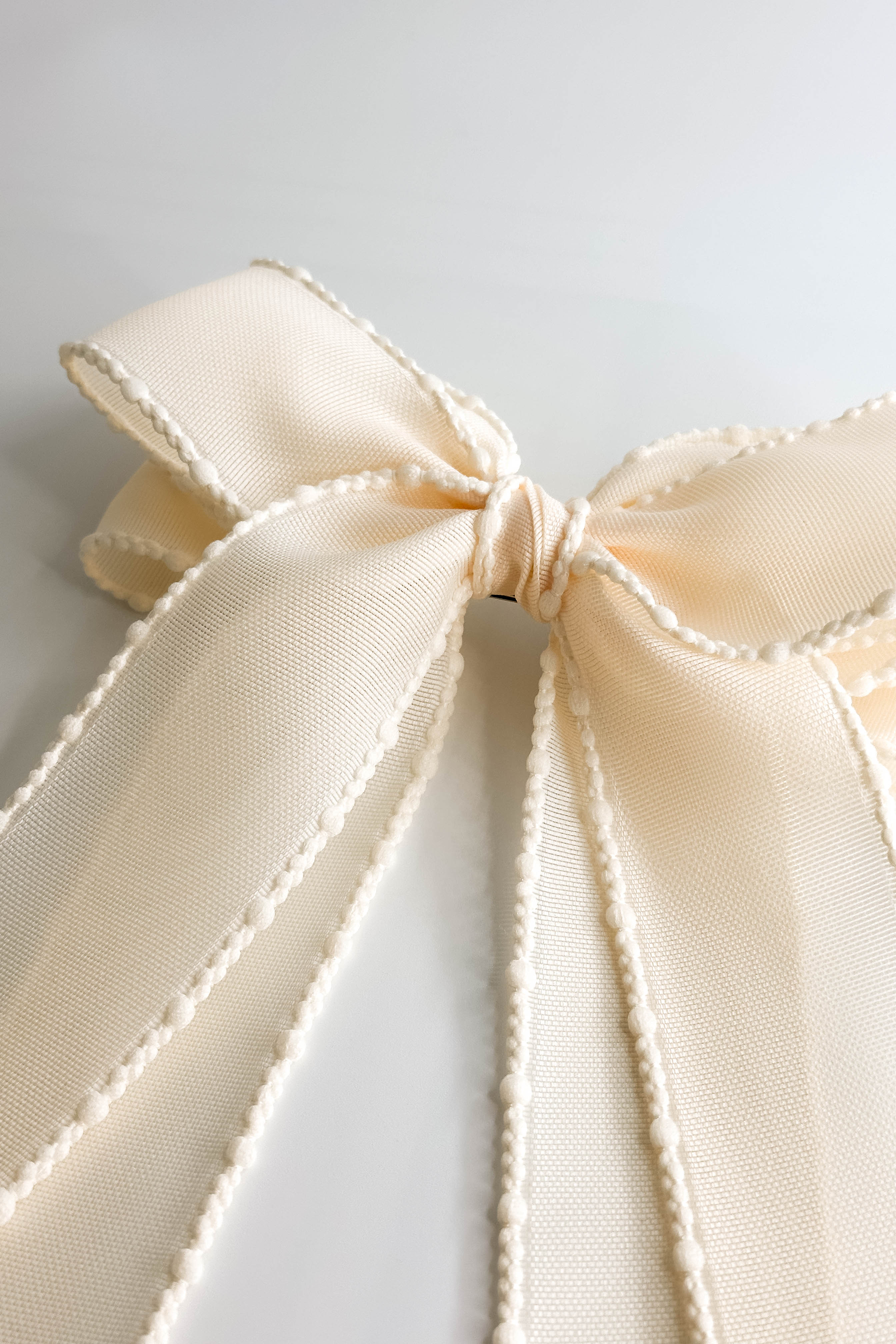 Close up view of the Harper Sheer Hair Bow Barrette in Ivory which features ivory sheer fabric, textured trim details, triple bow with a french barrette clip.