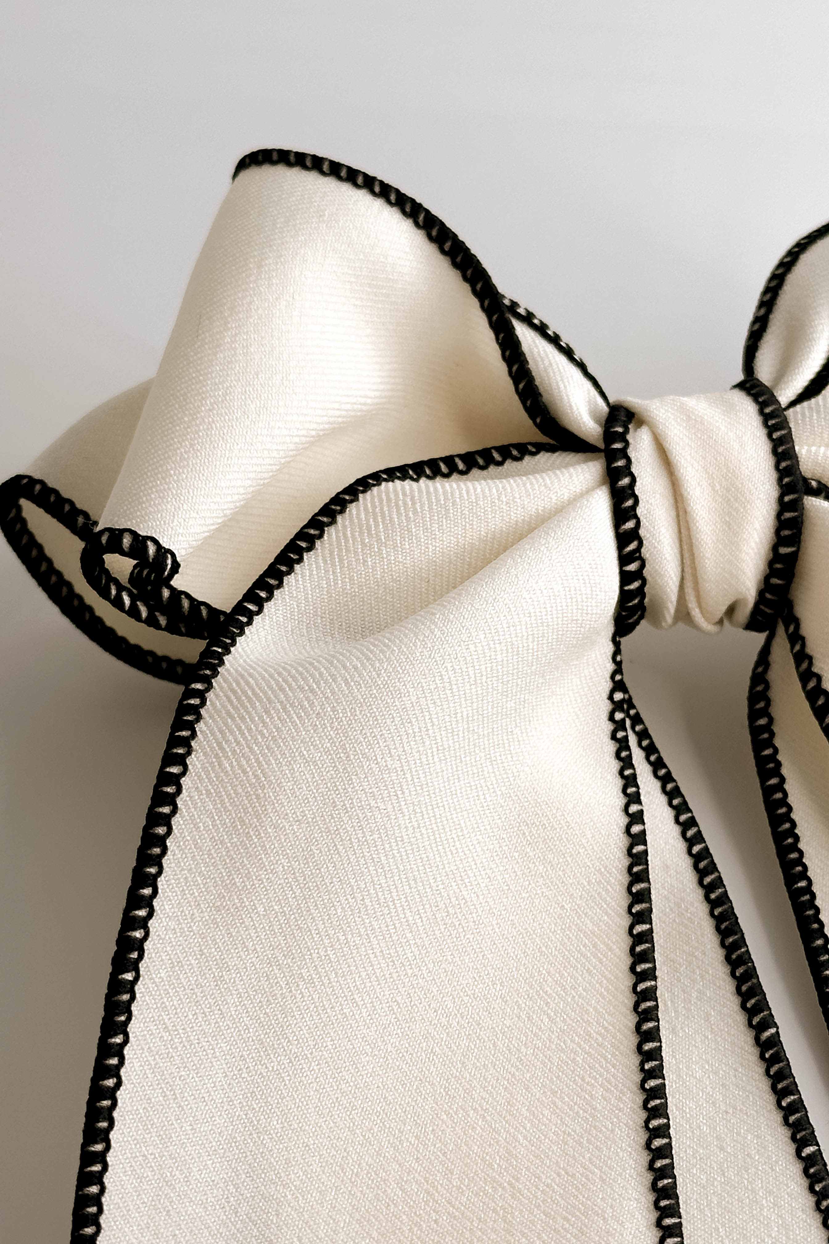 Close up view of Felicity Hair Bow Barrette in Ivory/Black which features ivory fabric with black fabric trim, double bow with a french barrette clip