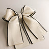 Flat lay view of Felicity Hair Bow Barrette in Ivory/Black which features ivory fabric with black fabric trim, double bow with a french barrette clip
