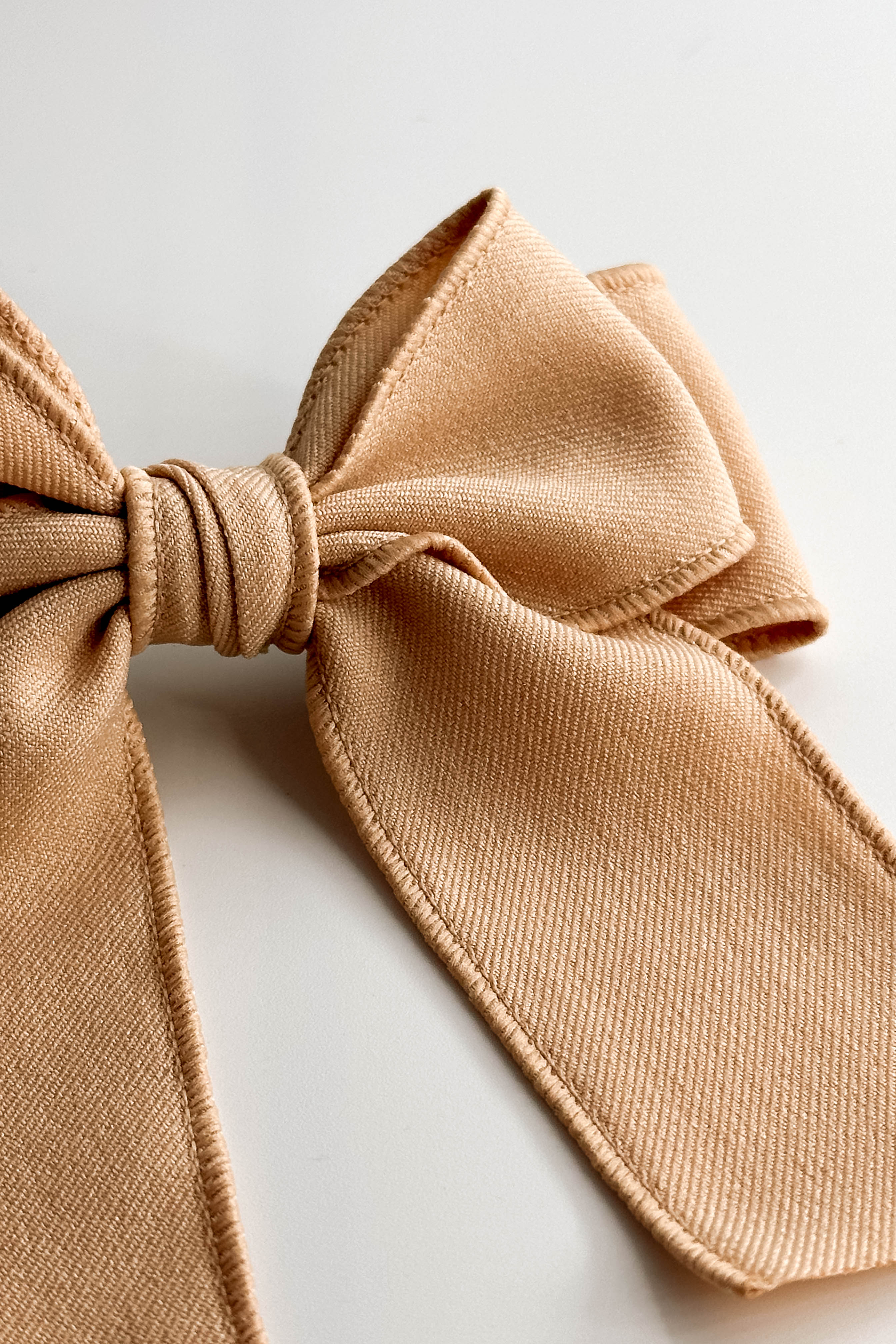 Close up view of the Olivia Hair Bow Barrette in Beige which features beige fabric, double bow with a french barrette clip