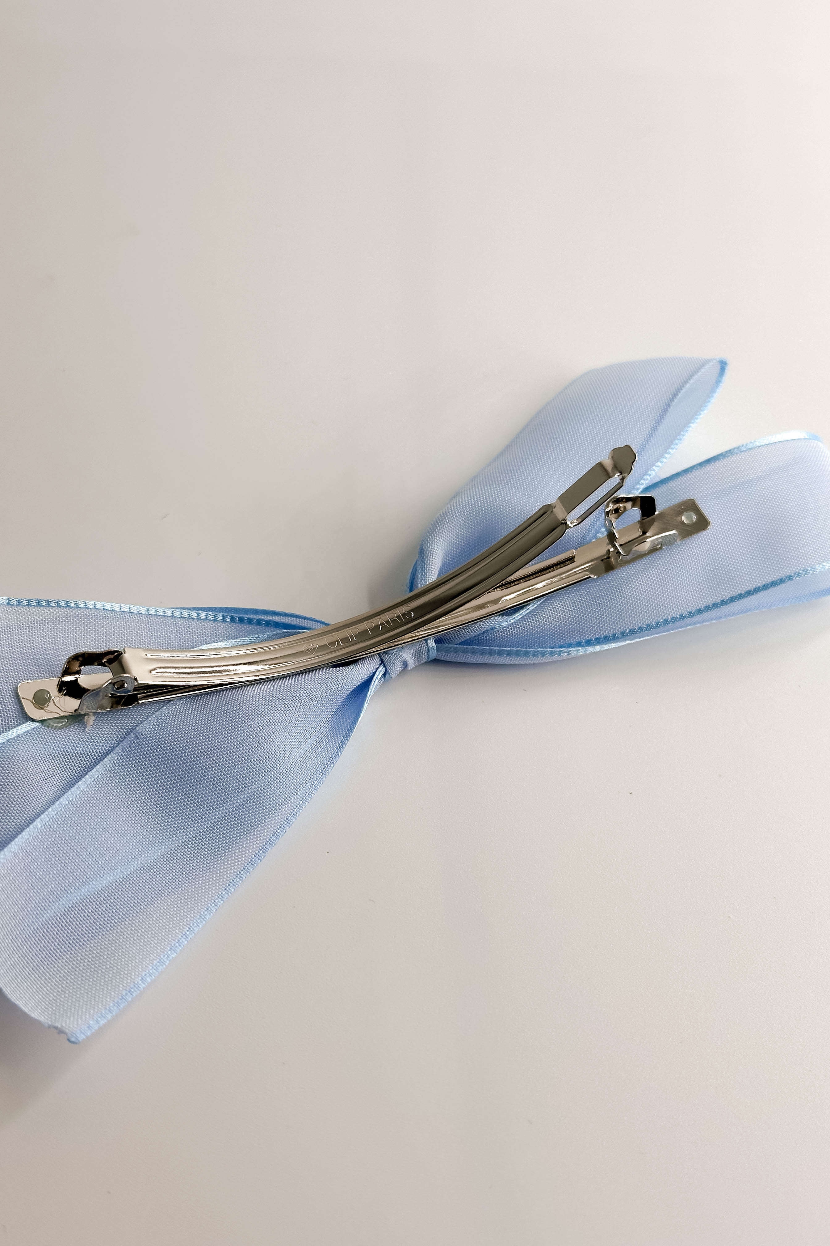 Back view of the Amelia Sheer Hair Bow Barrette in Light Blue which features light blue sheer fabric, light blue satin trim, double bow with a french barrette clip.