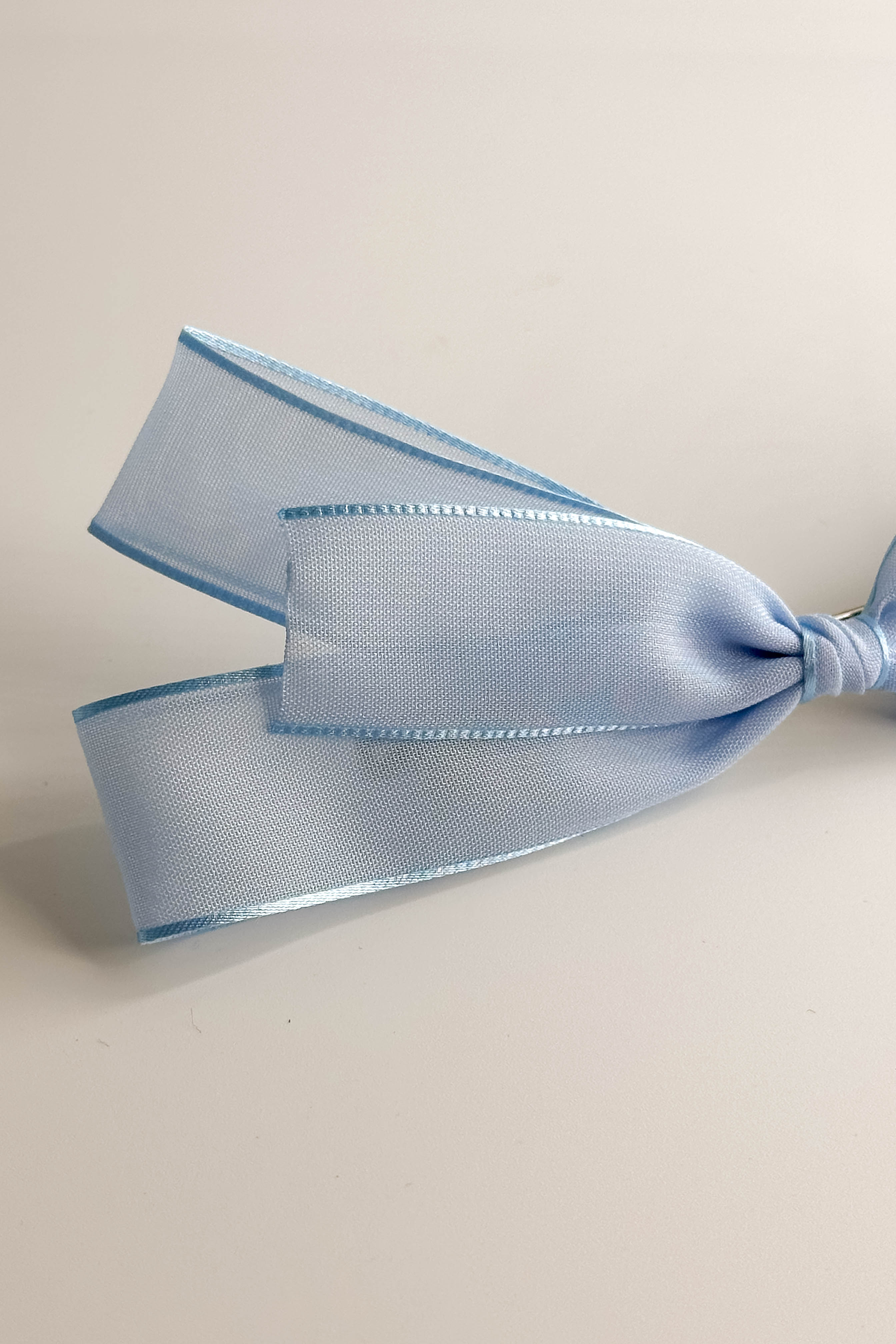 Close up view of the Amelia Sheer Hair Bow Barrette in Light Blue which features light blue sheer fabric, light blue satin trim, double bow with a french barrette clip.