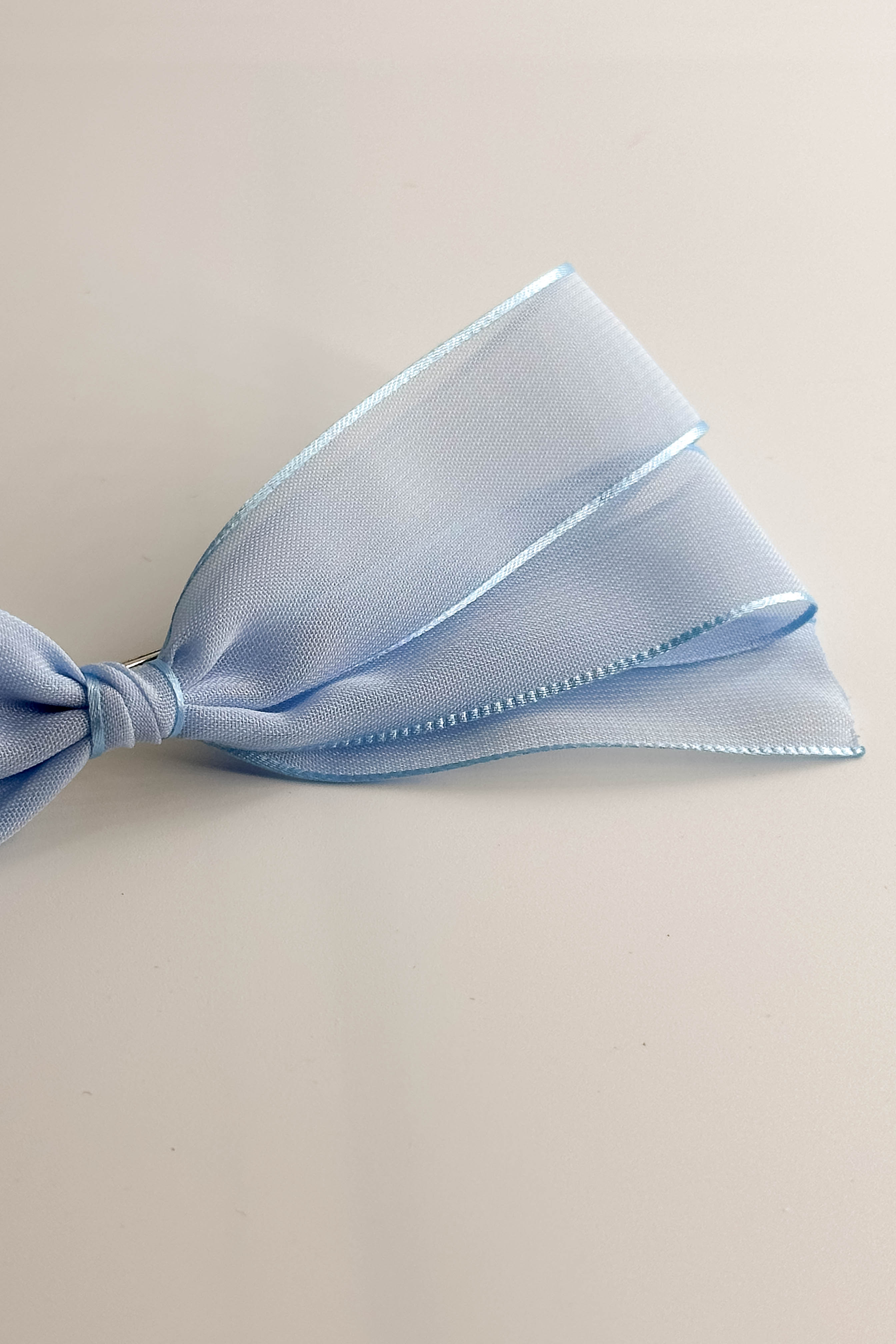 Close up view of the Amelia Sheer Hair Bow Barrette in Light Blue which features light blue sheer fabric, light blue satin trim, double bow with a french barrette clip.