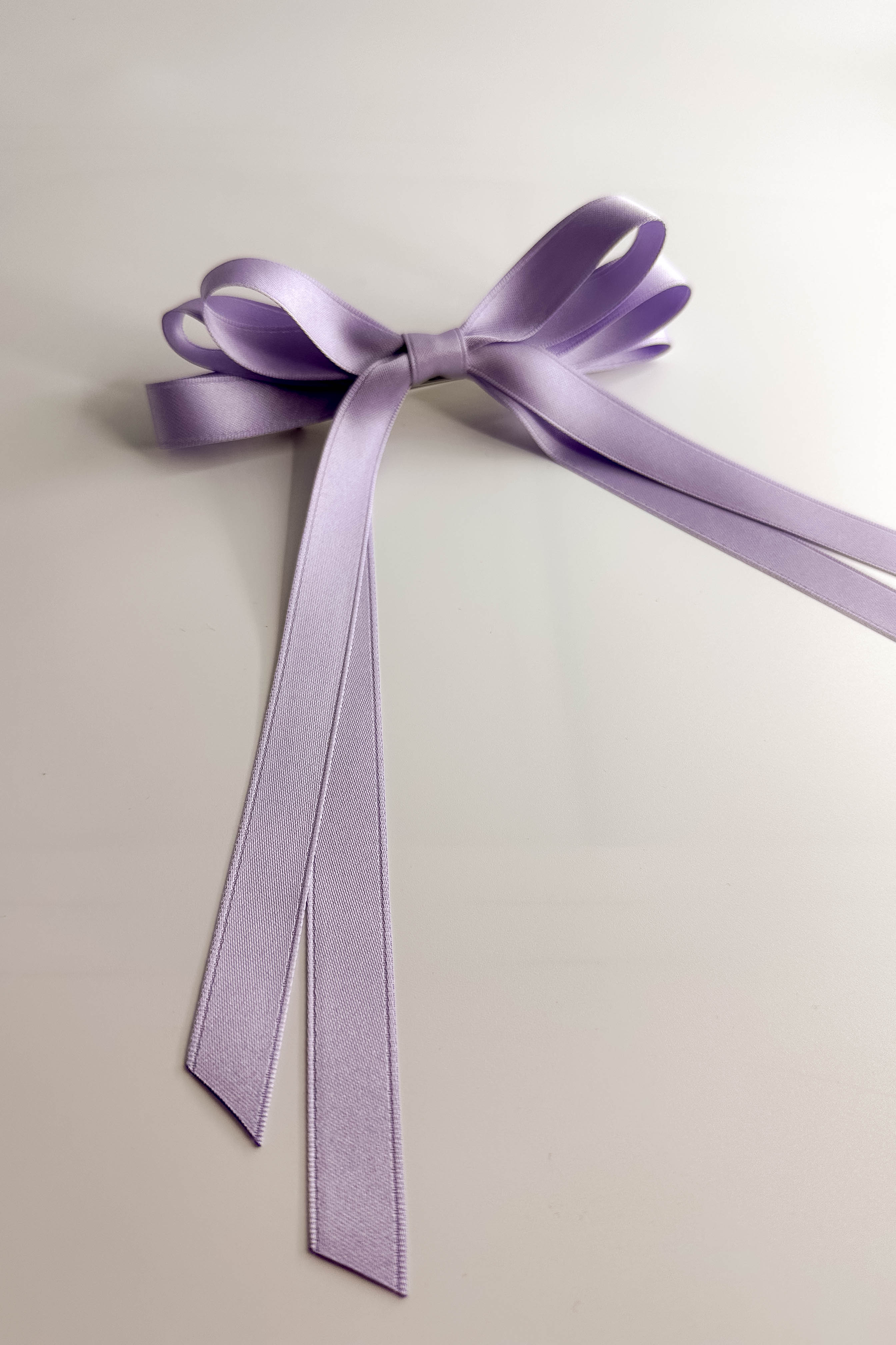 Flat lay view of Camila Satin Hair Bow Barrette in Lavender which features lavender, triple bow with a french barrette clip.