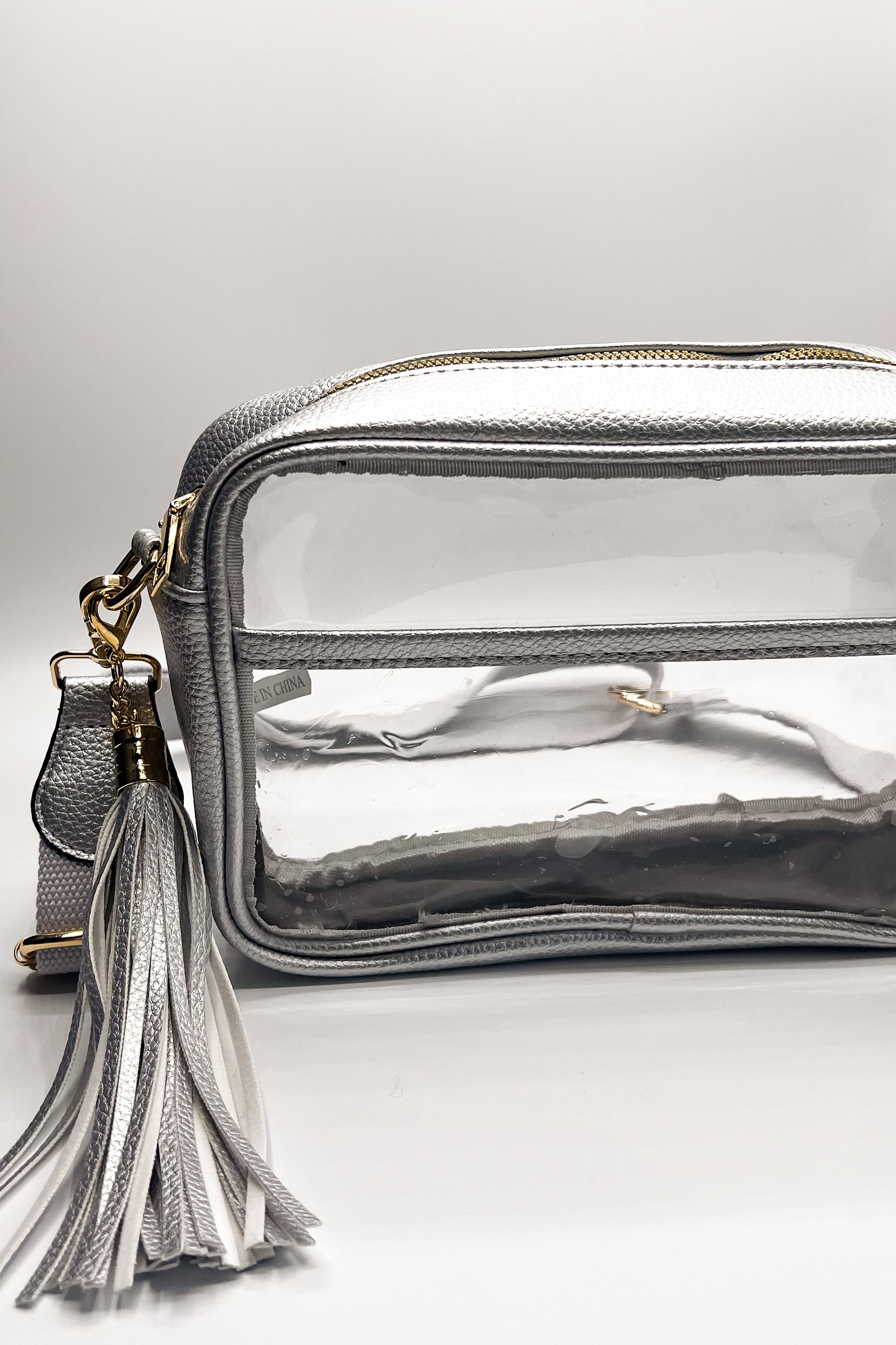 Image shows up close image of the Tiffany Clear Purse in Silver that has a clear rectangle body, silver exterior, a silver strap, and a silver fringe tassel.