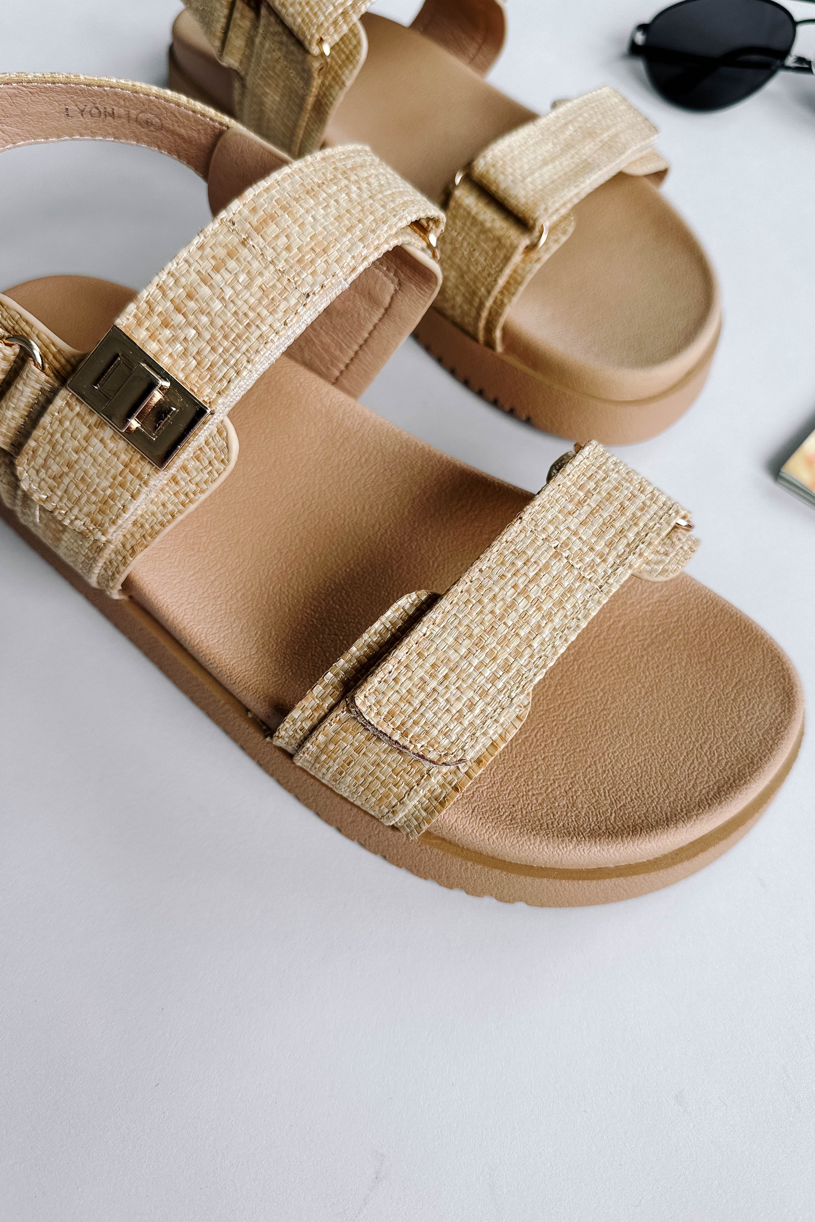 Close up view of the Lyon Sandal in Beige Raffia which features natural raffia fabric, two adjustable velcro straps, adjustable back strap and round toe.