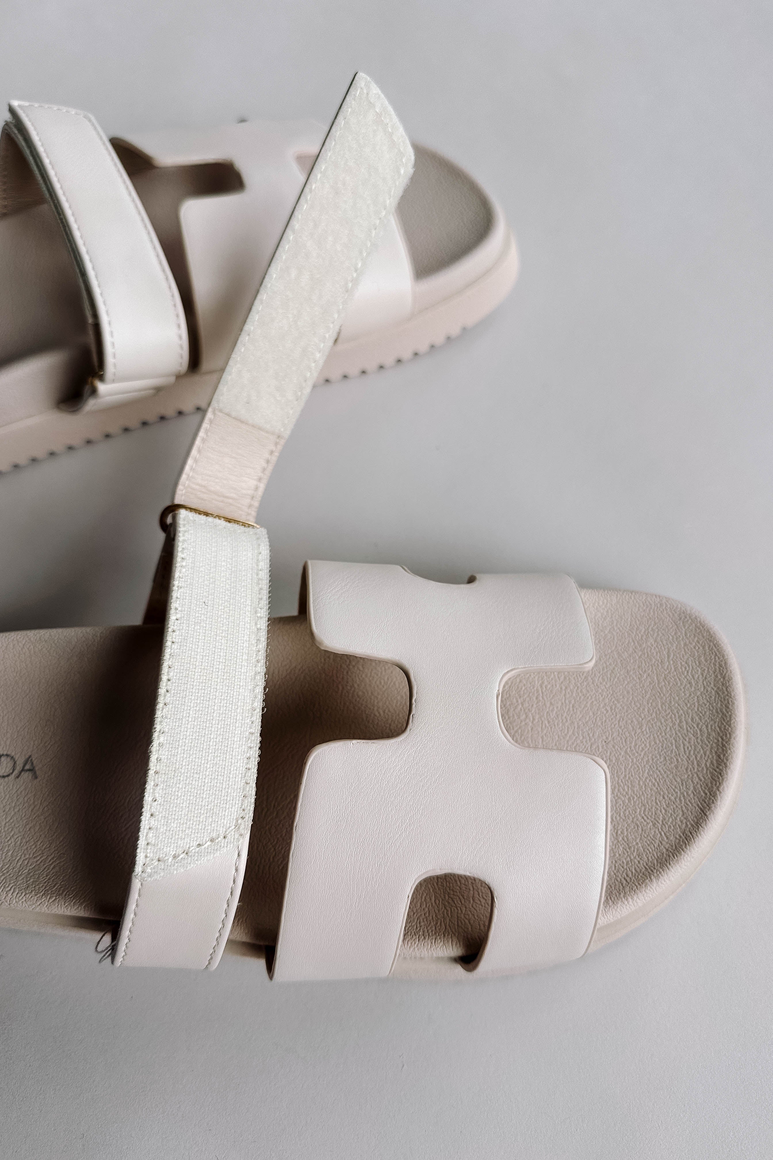Side view of the Jade Strap Sandal in Ivory which features ivory leather fabric, slide-on style, H-shaped strap, adjustable velcro strap and round toe.